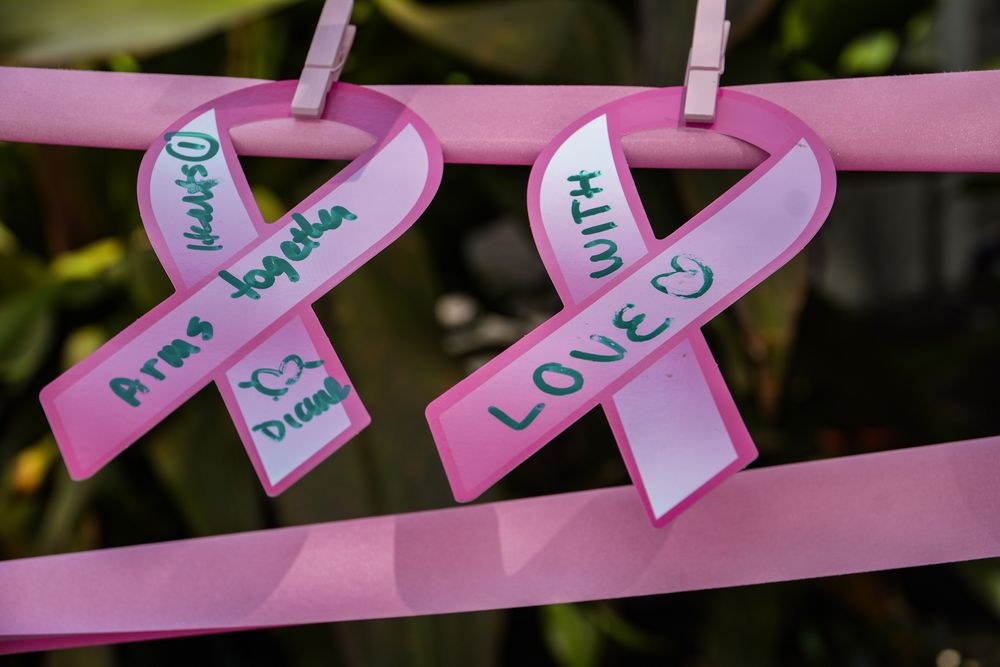 Two paper pink ribbons clipped to satin ribbon with handwritten messages reading "Arms together" and "with love", part of the Together In Community installation.