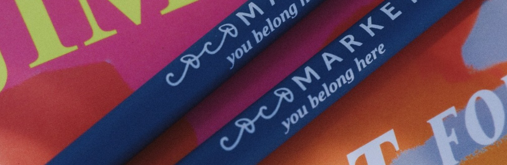 A stack of books with Coco Market bookmarks tucked inside, each printed with &lsquo;you belong here&rsquo;.