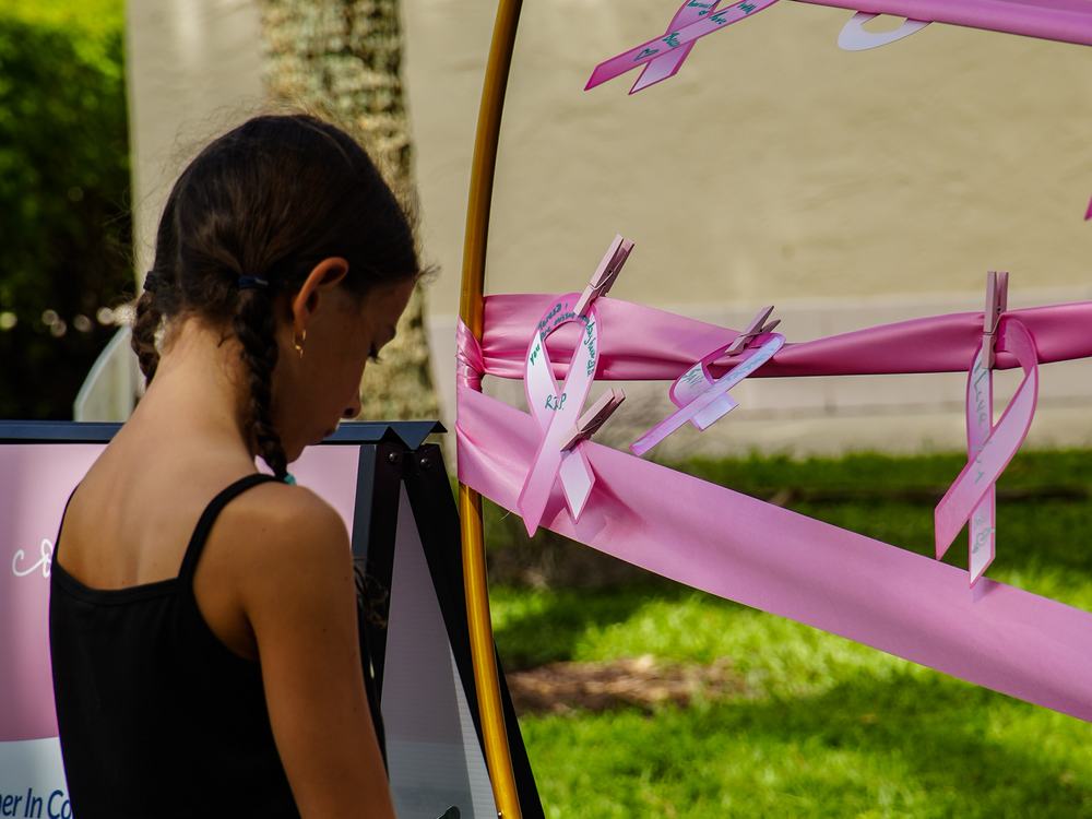 A visitor writing a loved one’s name on a pink ribbon at the remembrance station.